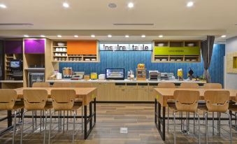 a cafeteria with wooden tables and chairs , a blue wall , and colorful bins on the shelves at Home2 Suites by Hilton Springdale Cincinnati