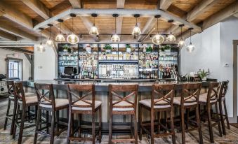 a bar with a wooden ceiling , stone flooring , and several chairs surrounding it , as well as bottles on the shelves at Briar Barn Inn