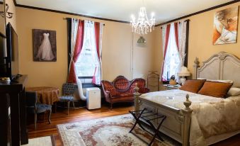 a cozy bedroom with hardwood floors , red curtains , and a large bed , as well as a chandelier hanging from the ceiling at Whole Hearts Bed and Breakfast