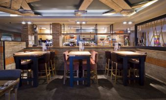 a modern restaurant with wooden tables , chairs , and a bar area , decorated with various items and people at Premier Inn Ware