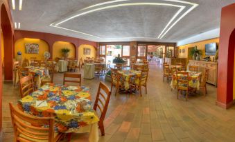 a large dining room with wooden tables and chairs , colorful tablecloths , and a mural on the ceiling at Hotel Hacienda