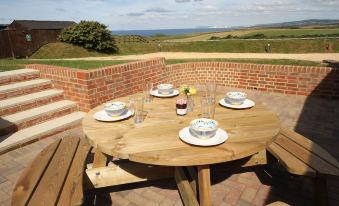 a wooden table with plates and glasses set for a meal on a patio overlooking the ocean at Chale Bay Farm