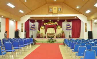 a large , empty event hall with rows of blue chairs and a stage in the background at Jazz Hotel Palu