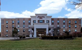 a large hotel building with a white facade and a red sign above the entrance at Hampton Inn-DeKalb (Near the University)