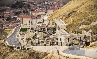 a small town with stone buildings and a church , situated on a hillside surrounded by trees at Kayakapi Premium Caves Cappadocia