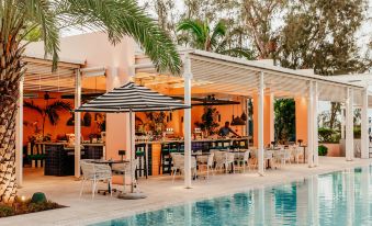 an outdoor dining area near a swimming pool , with several tables and chairs arranged around the pool at Salt of Palmar, Mauritius