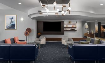 a modern living room with a large screen tv , blue and gray chairs , and a dark floor at Courtyard Los Angeles Burbank Airport