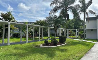 a lush green lawn with a white pergola in the background , surrounded by palm trees at Ramada by Wyndham Cocoa