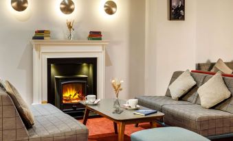 a cozy living room with two couches , a coffee table , and a fireplace , decorated with books and vases on the mantle at Mercure Telford Centre Hotel