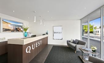a modern office reception area with a white desk and chairs , a couch , and a large window at Quest Cheltenham