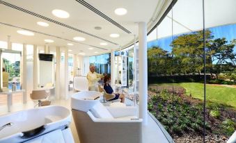 a modern living room with large windows offering a view of a garden , and people sitting on couches in the room at Racv Royal Pines Resort Gold Coast