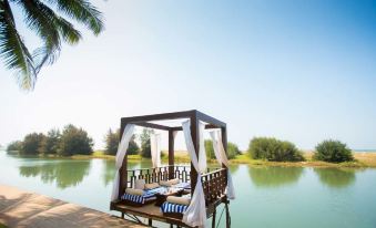 a wooden gazebo on a wooden platform with white curtains , situated near a body of water at Riva Beach Resort