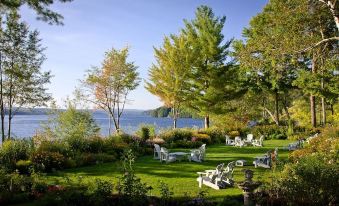 a serene backyard with a lake view , surrounded by lush green grass and trees , and white lawn chairs placed around the area at Manoir Hovey