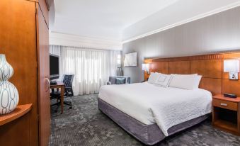 a modern hotel room with a white bed , wooden headboard , and gray carpet , along with a desk , chair , and window at Courtyard Danbury