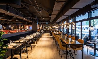 a modern restaurant with wooden floors , large windows , and black tables set for dining , along with yellow chairs and a bar in the background at Scandic Falkoner