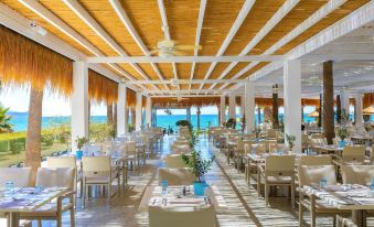 a large dining room with wooden tables and chairs , blue vases , and a view of the ocean at The GrandResort - Limited Edition by Leonardo Hotels