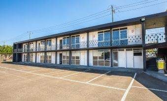 a modern apartment building with multiple floors , surrounded by trees and clear skies , and empty parking spaces at Nightcap at Westside Hotel