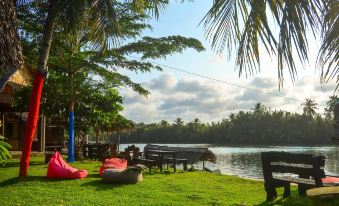 a serene scene of a lake with palm trees and a bench , with people relaxing on the grass at Shane Josa Resort