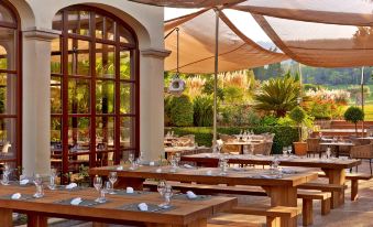 a restaurant with wooden tables and benches , surrounded by lush greenery and an outdoor patio at Sheraton Mallorca Arabella Golf Hotel