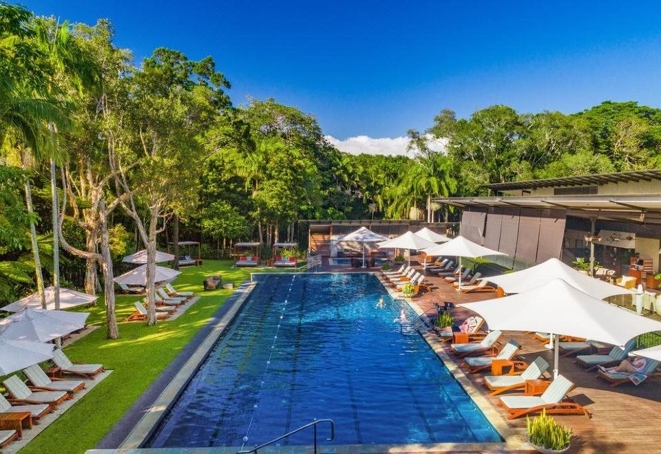 a large outdoor pool surrounded by lounge chairs and umbrellas , providing a relaxing atmosphere for guests at Crystalbrook Byron