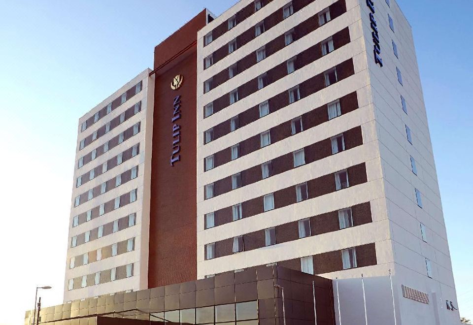 a tall white building with a brown and black facade , situated in front of a parking lot at Tulip Inn Itaguai