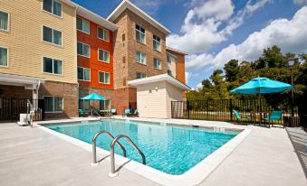 an outdoor swimming pool surrounded by a hotel building , with lounge chairs and umbrellas placed around the pool area at Residence Inn Greenville