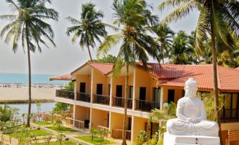 a large building surrounded by palm trees and a statue of a person sitting on a chair at Riva Beach Resort