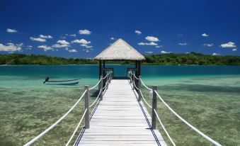 a wooden pier with a thatched roof , leading to a boat docked in the middle of a clear blue ocean at Eratap Beach Resort