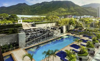 There is a large swimming pool with mountains in the background and a blue sky above it at Novotel Citygate Hong Kong