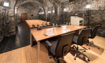 a conference room with wooden tables and black chairs arranged in rows , surrounded by stone walls and large windows at Grand Hotel Della Posta