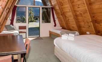 a room with two beds , one on each side of the room , and a dining table in the foreground at Wonderland Makarora Lodge