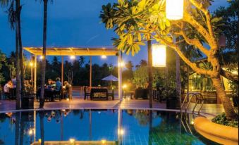 a well - lit swimming pool area at night , with several people enjoying their time in the pool at Baan Amphawa Resort & Spa