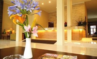 a vase with flowers is on a table in front of a reception desk and magazines at De View Hotel