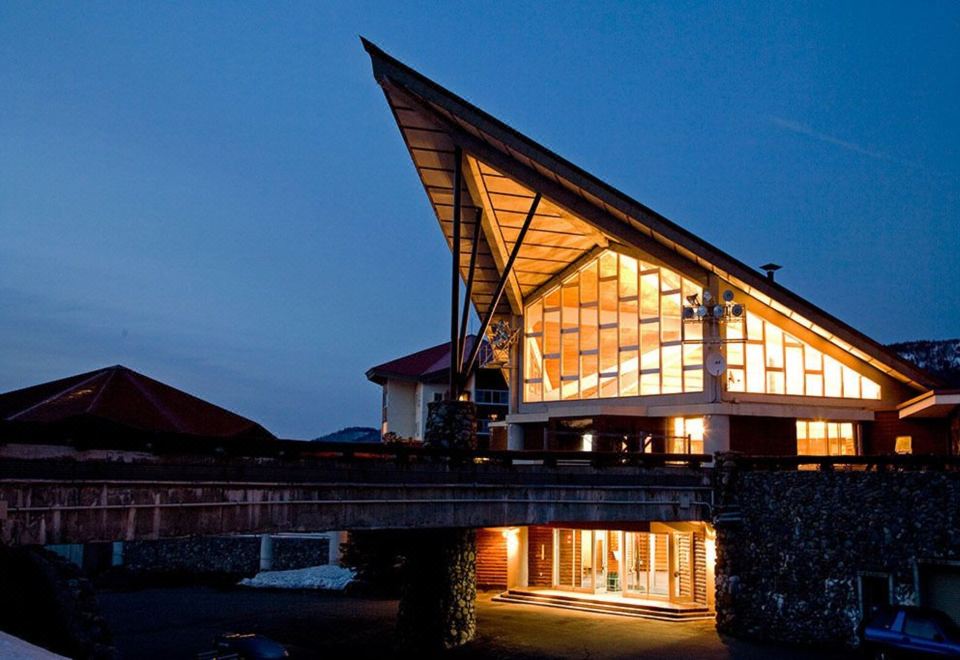 a modern , triangular - shaped building with a wooden roof and large windows at night , illuminated by lights at Okushiga Kogen Hotel