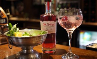 a bottle of st . giles gin , a wine glass filled with the gin , and a bowl of fruit salad on a wooden table at Recruiting Sergeant
