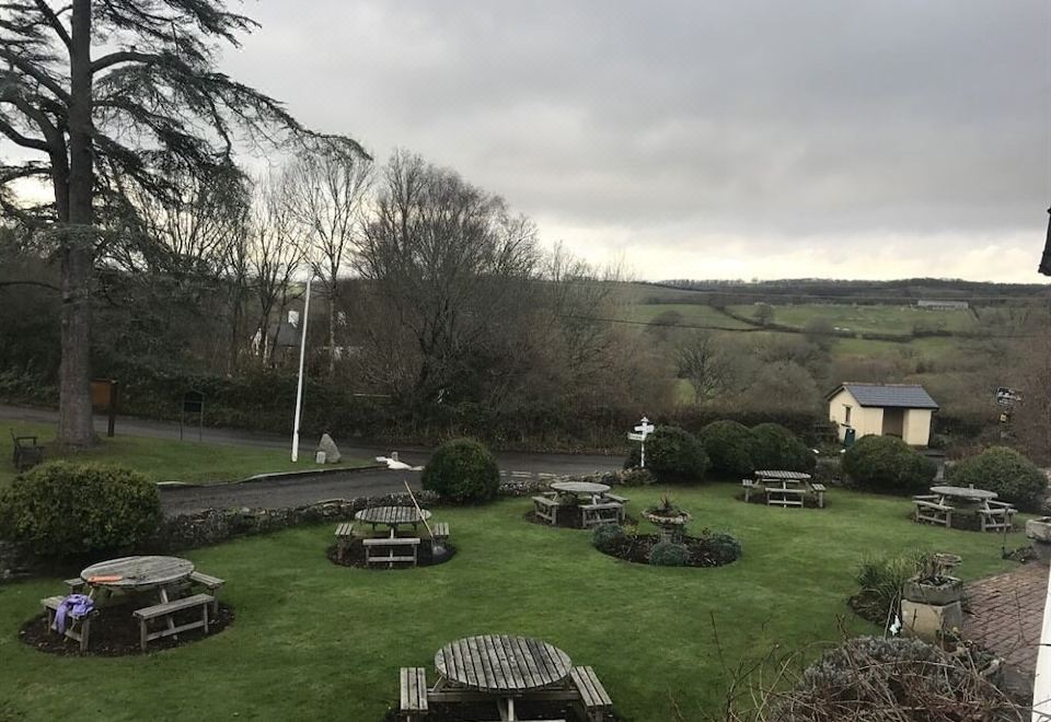 a large grassy field with multiple picnic tables and benches , surrounded by trees and hills at The Nobody Inn