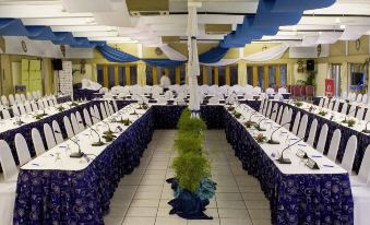 a large banquet hall with multiple rows of tables covered in blue tablecloths , where guests are seated and enjoying their meal at Novotel Suva Lami Bay