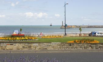 a picturesque view of the ocean with flowers , a stone wall , and a boat in the distance at Margate