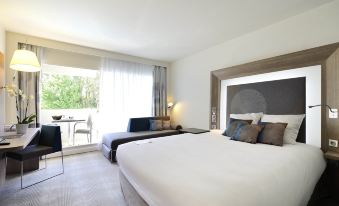 a modern hotel room with a large bed , couch , and sliding glass door leading to a balcony at Novotel Avignon Nord