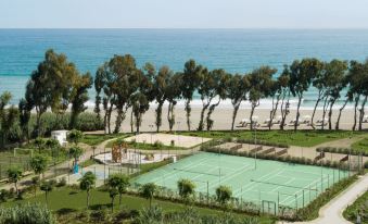 a tennis court is surrounded by a fence and trees , with the ocean in the background at Ikos Andalusia