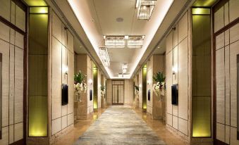 a long hallway with beige walls and a wooden floor , lined with potted plants and two blue signs at Crowne Plaza Lombard Downers Grove