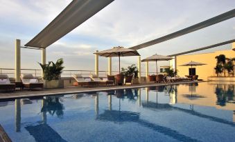 a large swimming pool with lounge chairs and umbrellas surrounding it , overlooking a balcony with palm trees at Taj Club House