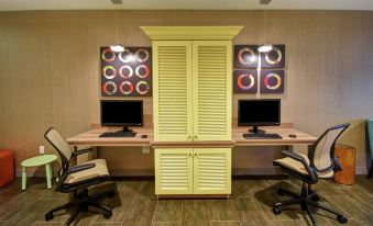 a room with two computer desks , each with a monitor and keyboard , and a cabinet in the background at Home2 Suites by Hilton Mechanicsburg