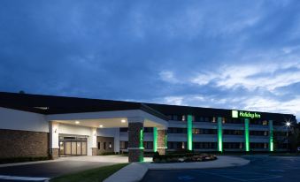 a holiday inn hotel at night , with its green and white exterior lit up against a dark sky at Holiday Inn Long Island - Islip Arpt East
