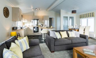 a modern living room with a gray couch and yellow pillows , next to a kitchen area at King's Lynn Caravan & Camping Park