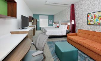 a hotel room with a bed , couch , desk , and tv , all decorated in white and blue at Home2 Suites by Hilton Hagerstown