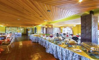 a long dining table filled with various food items , including plates , bowls , cups , and utensils at Rainbow Ruiru Resort