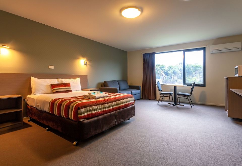 a modern hotel room with a large window , red striped bedspread , and black furniture , along with some text indicating the hotel 's name at Kingston Hotel Motel