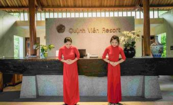 "two women in red dresses stand at a reception desk with a sign that says "" quoi phan vieh resort .""." at Quynh Vien Resort Ha Tinh