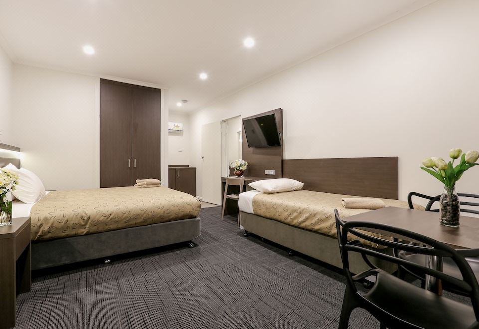 a modern hotel room with two beds , a desk , and a tv , all neatly arranged at Morphettville Motor Inn